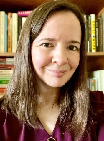 A headshot of Jessica Vitak with a bookshelf full of books behind her. She has on a burgundy top and her hair is brown.