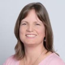 headshot of jean snell, a gray background, she is wearing a pink top
